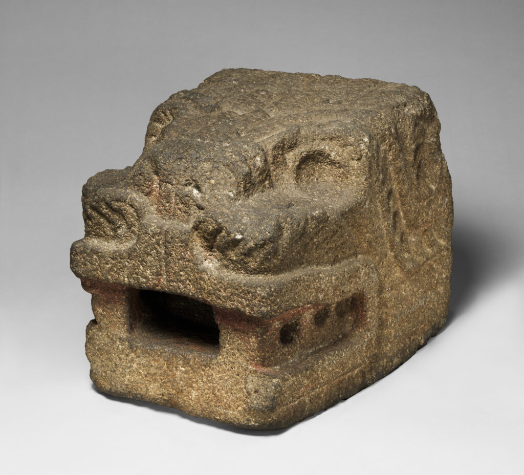 Stone sculpture of a feathered serpent head from Teotihuacan, mouth open and teeth bared, with feathers carved in low relief on the snout and around the eyes. 100–500 CE, Metropolitan Museum of Art.
