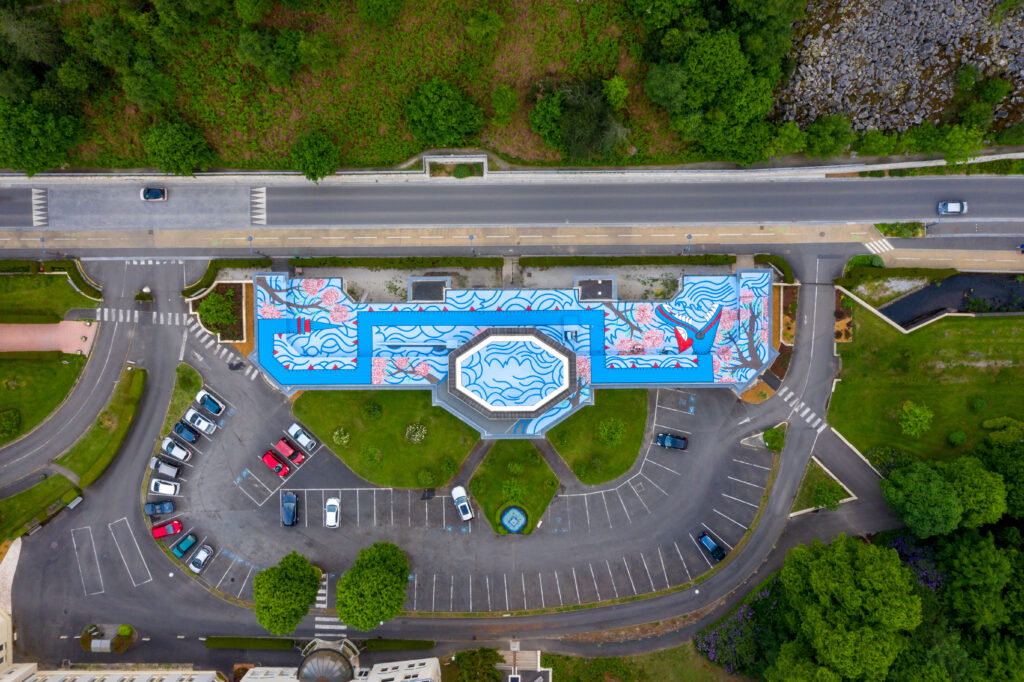 Vertical aerial view of the Pavillon des Fleurs, Bagnoles-de-l'Orne, showing the full extent of Oré's Quetzalcoatl roof mural in its urban context, 2022.