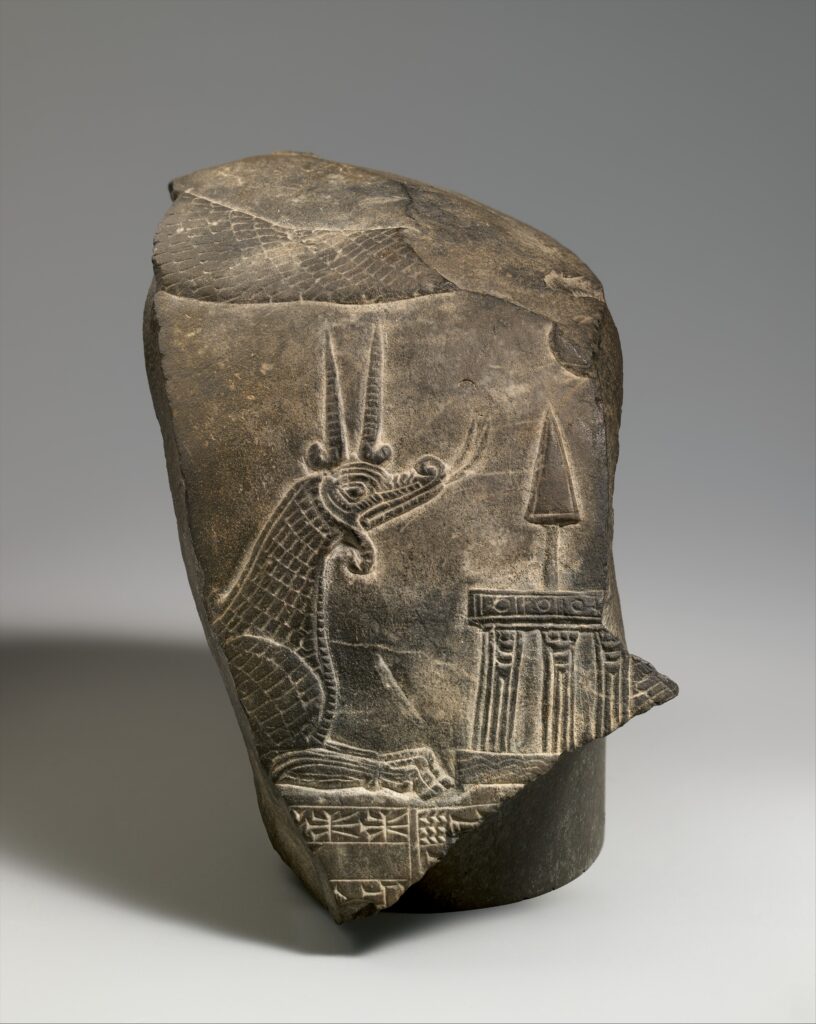 Carved limestone fragment showing a horned, scaled dragon with lion forelegs beneath a temple façade symbol, with a snake's body coiling along the stone's upper edge.